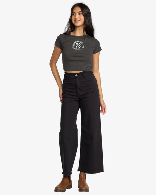 Woman wearing a dark gray t-shirt and billabong free fall black pants on a white background