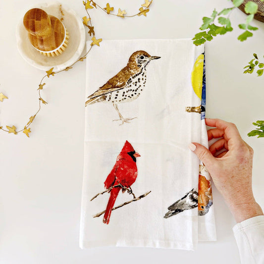 Towel with bird designs held by a hand on a white surface with decorative elements.