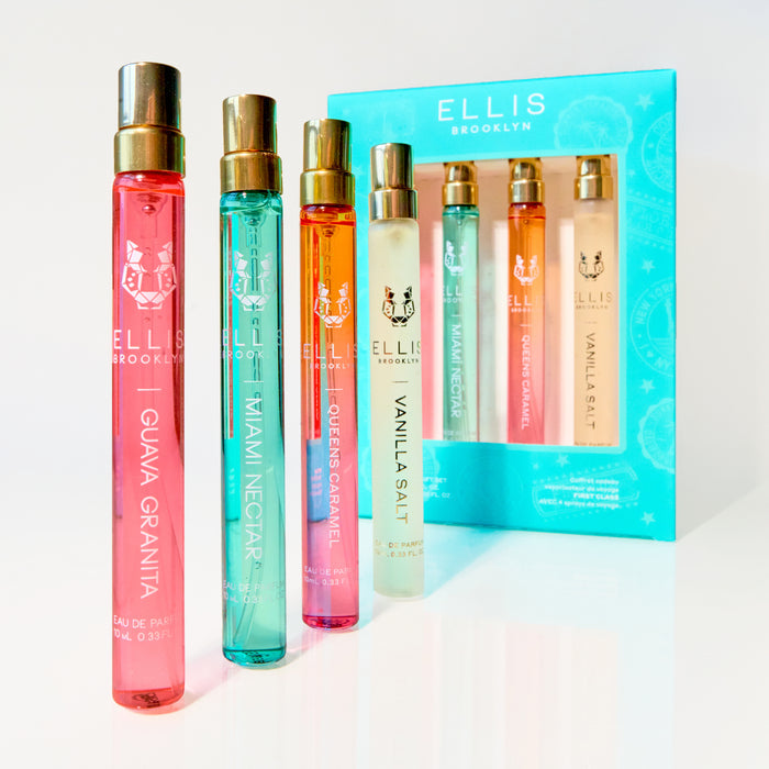 FIRST CLASS Gift Set containing GUAVA GRANITA Eau de Parfum 10ml, MIAMI NECTAR Eau de Parfum 10ml, QUEENS CARAMEL Eau de Parfum 10ml, and VANILLA SALT Eau de Parfum 10ml next to  standing GUAVA GRANITA Eau de Parfum 10ml, MIAMI NECTAR Eau de Parfum 10ml, QUEENS CARAMEL Eau de Parfum 10ml, and VANILLA SALT Eau de Parfum 10ml all on a white surface and background