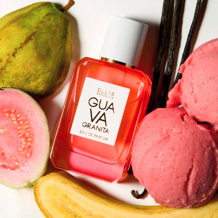 GUAVA GRANITA Eau de Parfum 50ml lays next to a guava, half a sliced guava, a sliced banana, two scoops of pink granita, and 3 vanilla beans on a white background