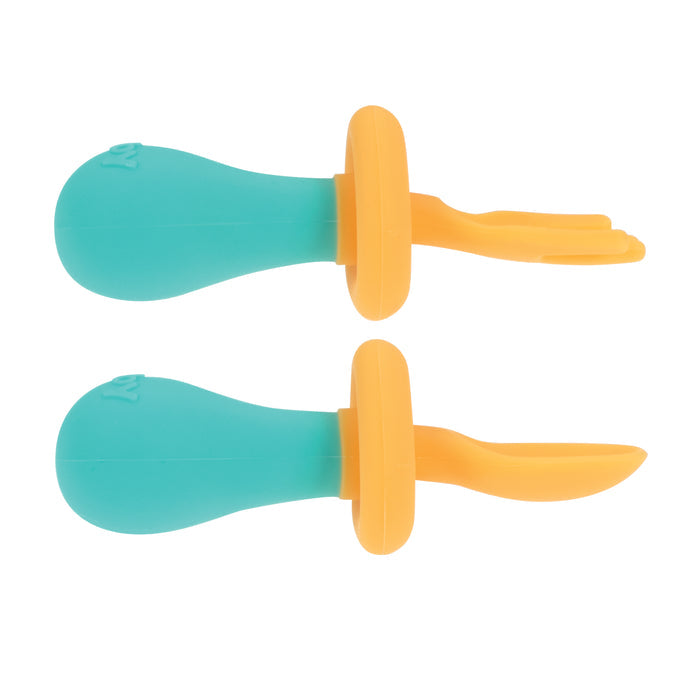 The First Fork & Spoon Set includes two self-feeding utensils: a three-prong fork and a spoon, both with teal handles, orange silicone tips, and built-in safety guards to help prevent choking.