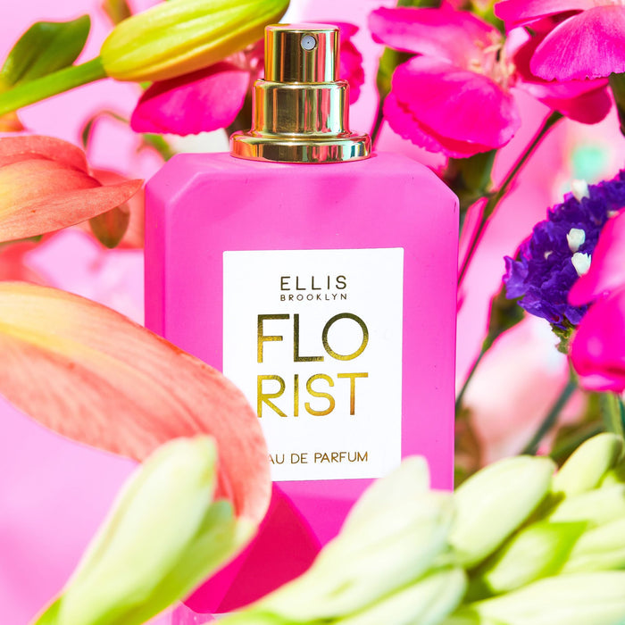 Florist 50ml Eau De Parfum with cap removed on pink background surrounded by pink, green, yellow, orange, and purple flowers.