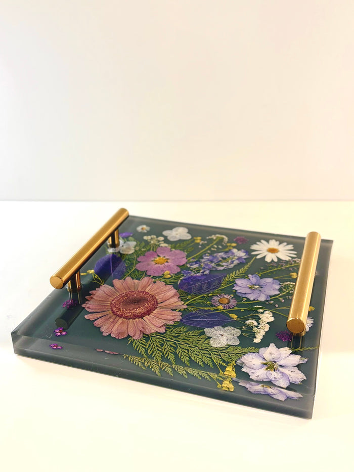 Decorative tray with floral design and gold handles on a white background. Square clear resin tray featuring a beautiful arrangement of embedded dried yellow and red flowers with metallic accent handles.