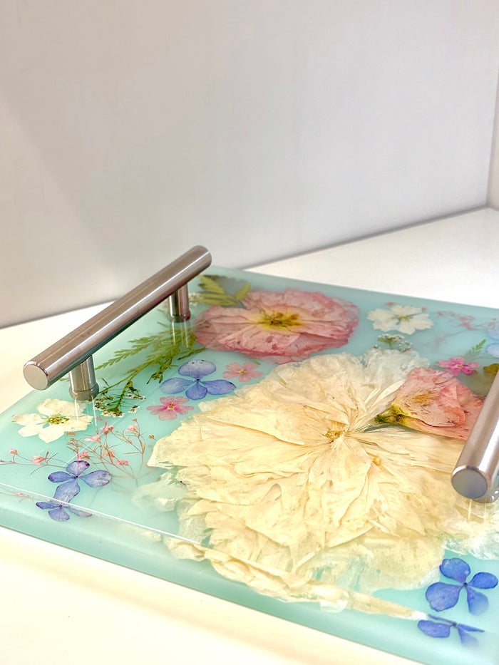 Decorative glass tray with floral design and metal handles on a white surface.