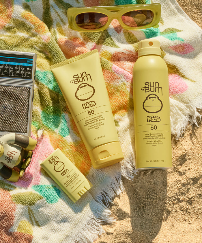 Sun Bum Kids sunscreen products on a colorful towel with sunglasses and a radio.