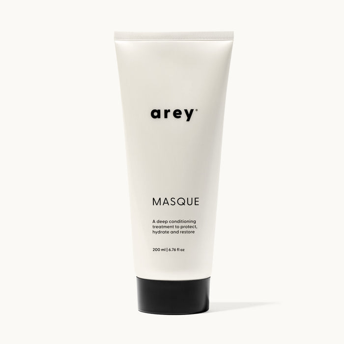 Product shot of arey Masque tube on a white/cream background. Label reads: arey® MASQUE. "A deep conditioning treatment to protect, hydrate and restore." 200 ml | 6.76 fl oz.