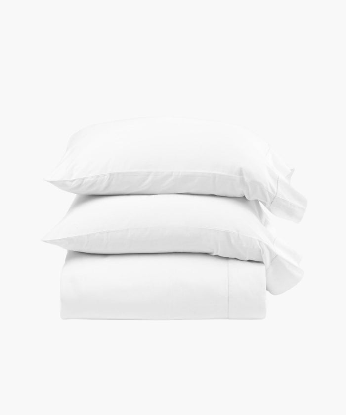 Stacked display of the Murano white sheet set including pillowcases, a fitted sheet, and flat sheet, showcasing the clean lines and smooth cotton sateen finish. | Wildwood Home Co.