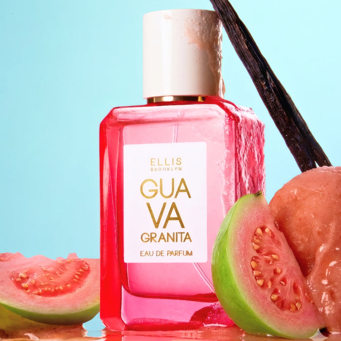 GUAVA GRANITA Eau de Parfum 50ml with a vanilla bean leaning against the cap sits on reflective surface between slices of cut guava all covered in water droplets on a blue background.
ge