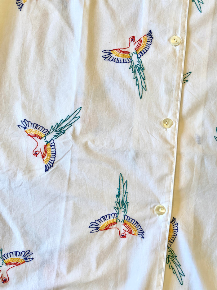 White shirt with colorful bird embroidery on a beige background