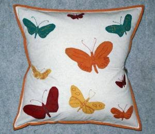 A square decorative pillow with colorful embroidered applique of butterflies on a white background with an orange trim.